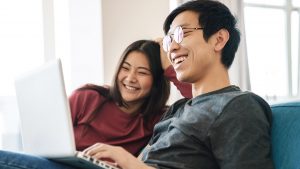 Cheerful young asian couple sitting on a couch at home, using la